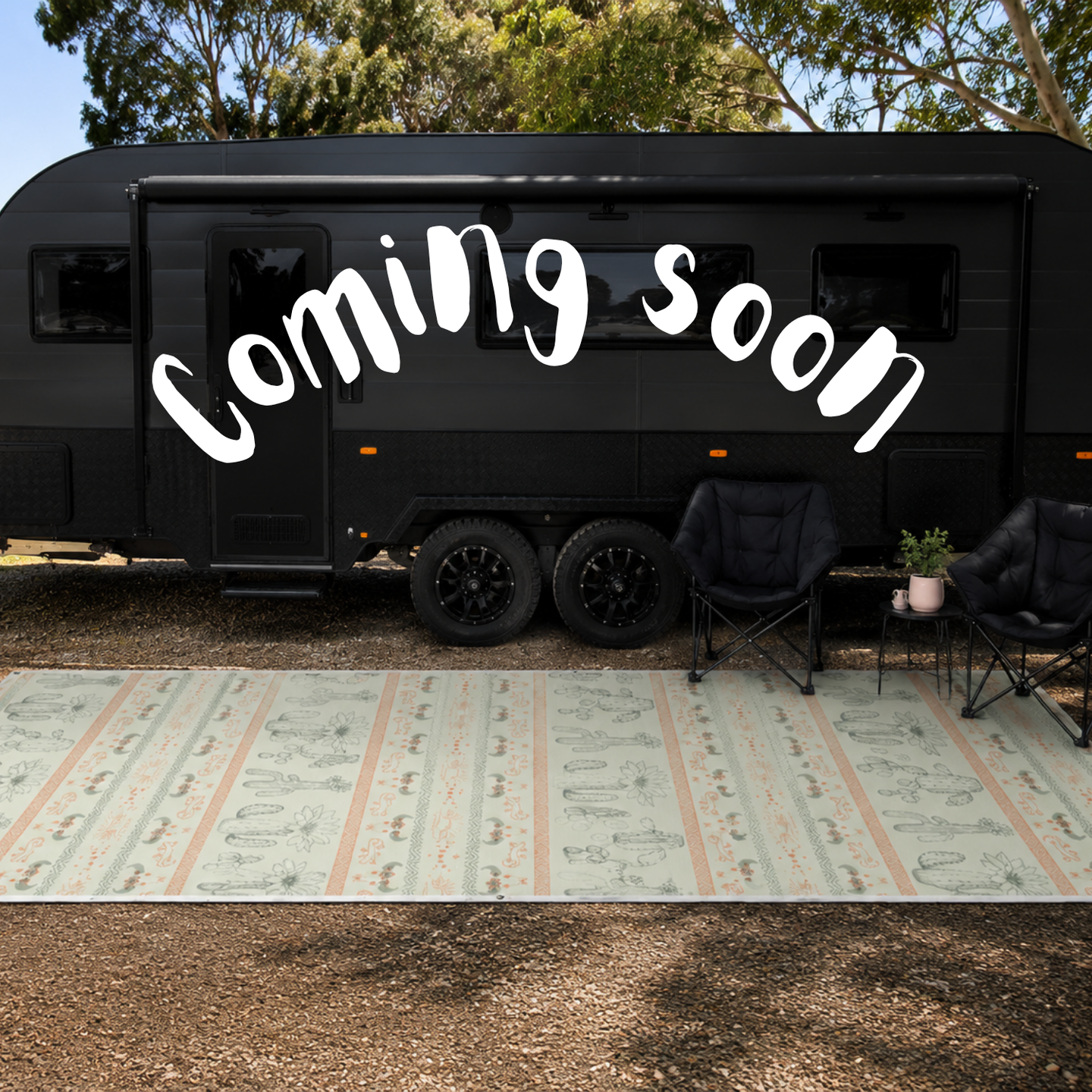 A black caravan parked outdoors on a gravel surface with a green camping recycled mat  two black camping chairs, and a small side table. Large white text reading 'Coming soon' is overlaid across the trailer.
