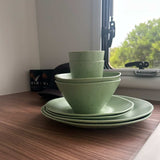 Stack of Speckled green rPET bowls and plates on a wooden caravan surface with a window in the background. asymmetrical dinnerware