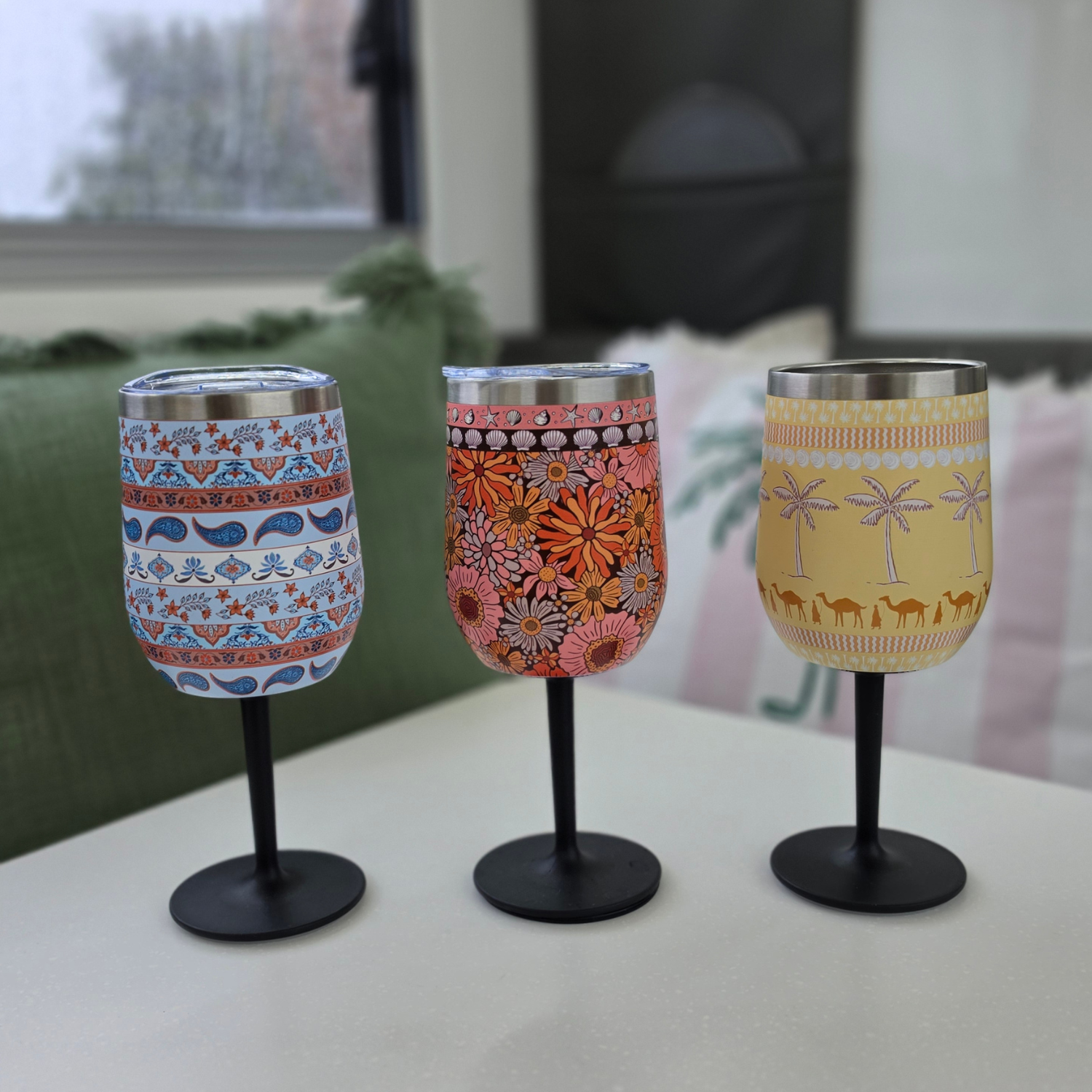 Three Vanaway insulated stainless steel wine tumblers with removable screw-on stems, featuring the Blue Paisley, Sunblossom and Golden Palms designs displayed side by side. caravan table