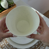 Close-up of the Vanaway Speckled Coconut white rPET bowl held in both hands, showcasing its generous depth, smooth matte finish and subtle grey speckled pattern. asymmetrical dinnerware