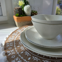 Close-up of the Vanaway Speckled Coconut rPET caravan dinnerware set, featuring stacked dinner plates, side plates and bowls with a soft white speckled finish. asymmetrical dinnerware