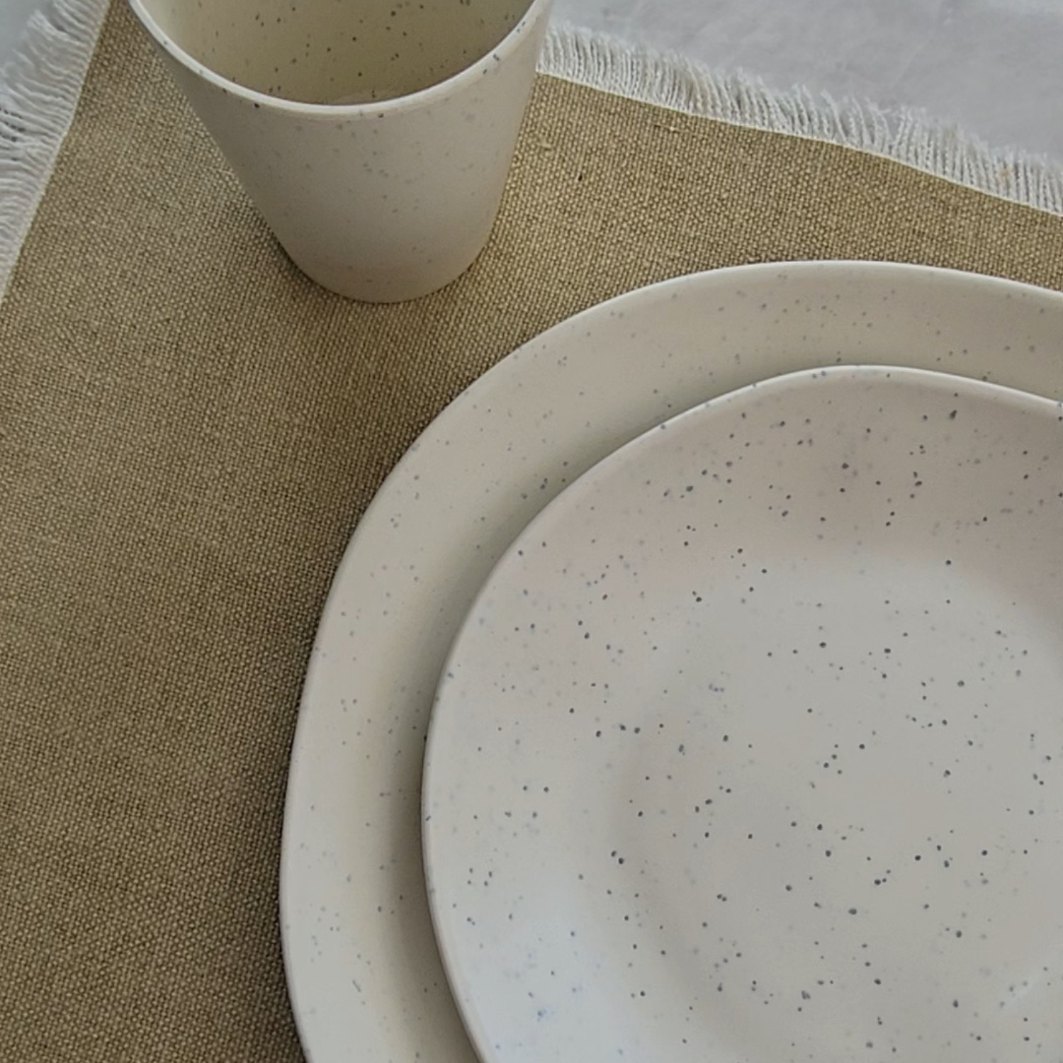 Close-up of the Vanaway Speckled Coconut rPET caravan dinnerware, featuring the speckled white dinner plate, side plate and tumbler to showcase the premium matte finish and subtle recycled texture. asymmetrical dinnerware
