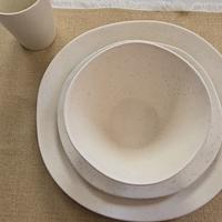Overhead flat lay of Vanaway Speckled Coconut white rPET dinnerware including a dinner plate, side plate, bowl and cup, styled on a natural linen table runner to showcase the subtle speckled finish. asymmetrical dinnerware