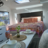 Speckled Coconut white rPET caravan dinnerware styled on a caravan table with matching wine tumbler, indoor plant and Dahlia woven throw rug on the bed, showcasing a practical and stylish vanlife setup. asymmetrical dinnerware