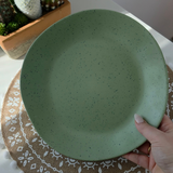 Close-up of the Vanaway Speckled Matcha rPET dinner plate in sage green with a black speckled finish, shown in hand to highlight its generous size and matte texture. asymmetrical dinnerware
