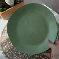 Close-up of the Vanaway Speckled Matcha rPET dinner plate in sage green with a black speckled finish, shown in hand to highlight its generous size and matte texture. asymmetrical dinnerware