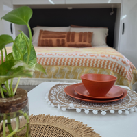 Vanaway Speckled Spice rPET caravan dinnerware place setting on a caravan table, with the Vanaway Solana Throw Rug styled on the bed in the background to create a warm, coordinated camping setup. asymmetrical dinnerware