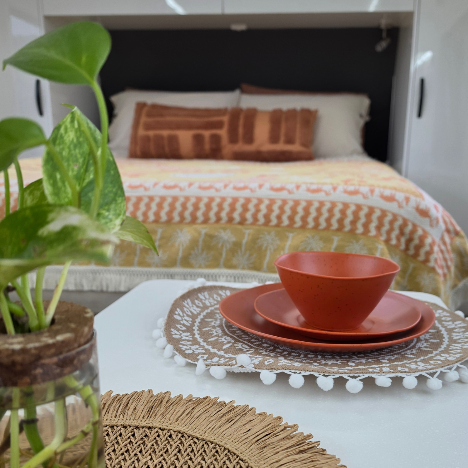 Vanaway Speckled Spice rPET caravan dinnerware place setting on a caravan table, with the Vanaway Solana Throw Rug styled on the bed in the background to create a warm, coordinated camping setup. asymmetrical dinnerware
