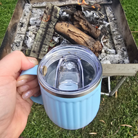 Hand holding a blue mug with a clear lid over a campfire