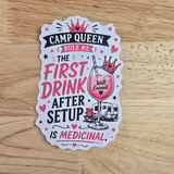 A die-cut camp queen sticker from vanaway with a humorous camping slogan, displayed flat on a light wood background. The sticker features a white base with pink, black, and red illustrations, including a crown, a cocktail glass with a pink drink, a small trailer, and the text 'CAMP QUEEN RULE #2: THE FIRST DRINK AFTER SETUP IS MEDICINAL.