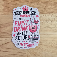 A die-cut camp queen sticker from vanaway with a humorous camping slogan, displayed flat on a light wood background. The sticker features a white base with pink, black, and red illustrations, including a crown, a cocktail glass with a pink drink, a small trailer, and the text 'CAMP QUEEN RULE #2: THE FIRST DRINK AFTER SETUP IS MEDICINAL.