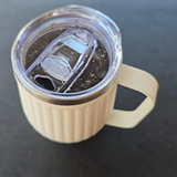 White insulated camp mug with handle with a clear lid on a dark surface