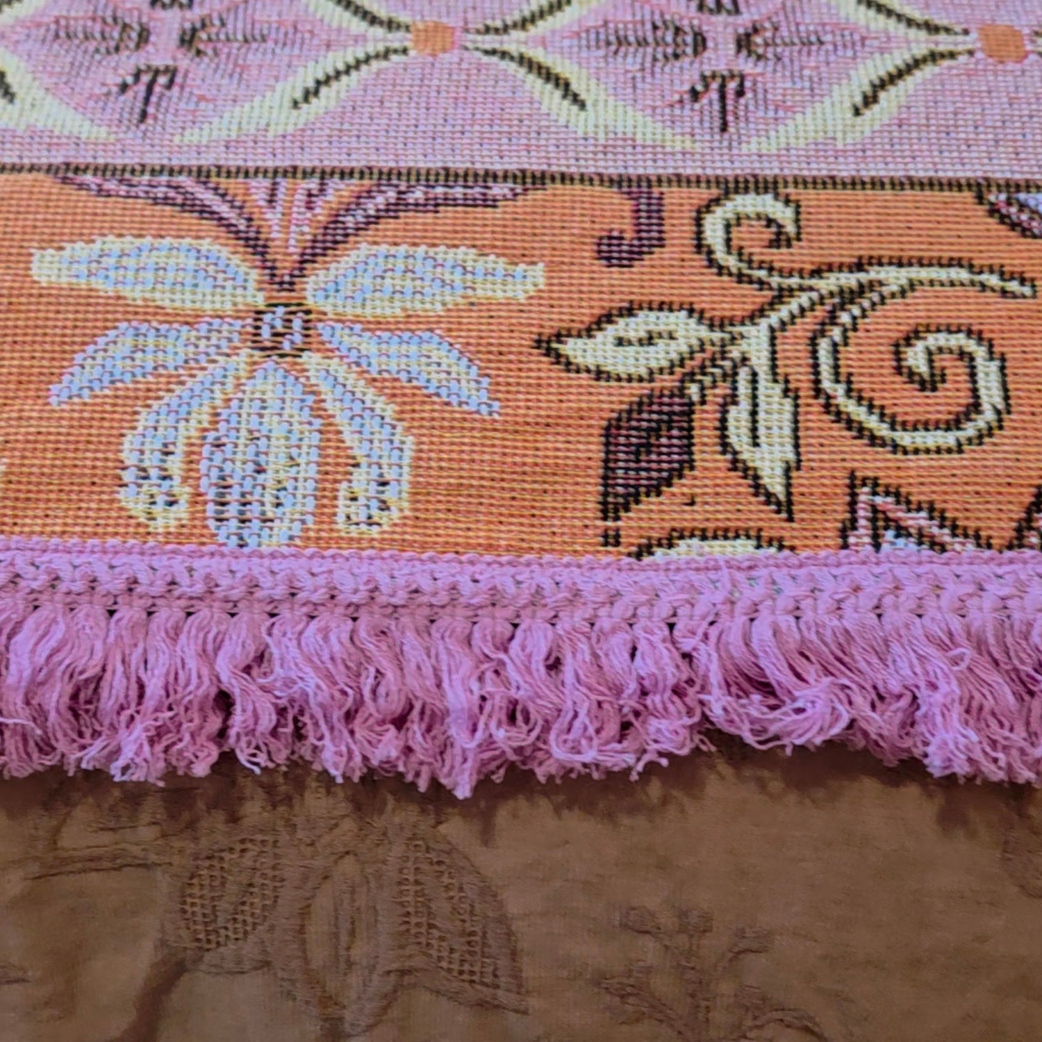 Close up of the Vanaway Dahlia woven travel throw rug showcasing its pink decorative fringe, terracotta border and premium woven cotton texture.
