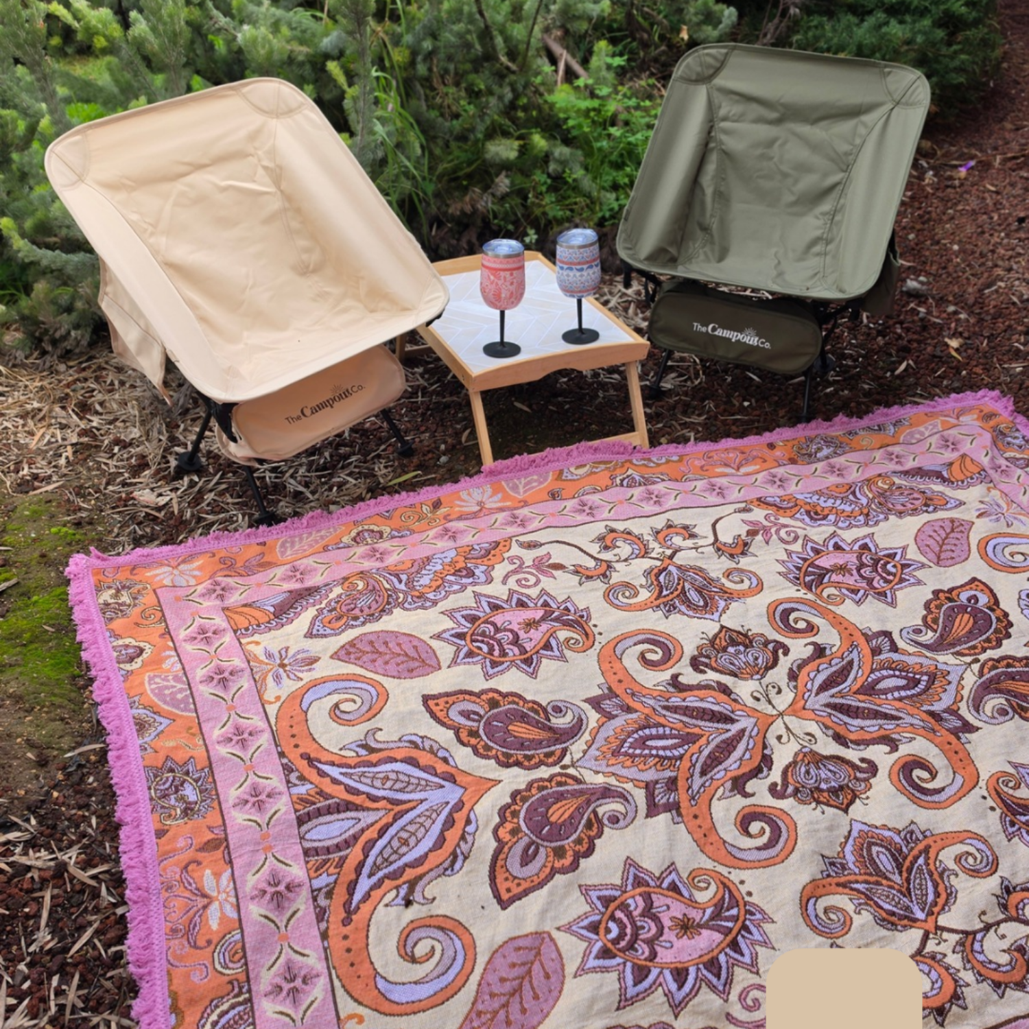 Vanaway Dahlia woven travel throw rug featuring a cream, lilac, lavender and terracotta boho paisley design, styled with camping chairs and insulated drinkware in a peaceful bush camping setting.