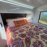 Vanaway Dahlia woven travel throw rug featuring a cream, lilac, lavender and terracotta boho paisley design, styled as a decorative bed throw inside a modern caravan.