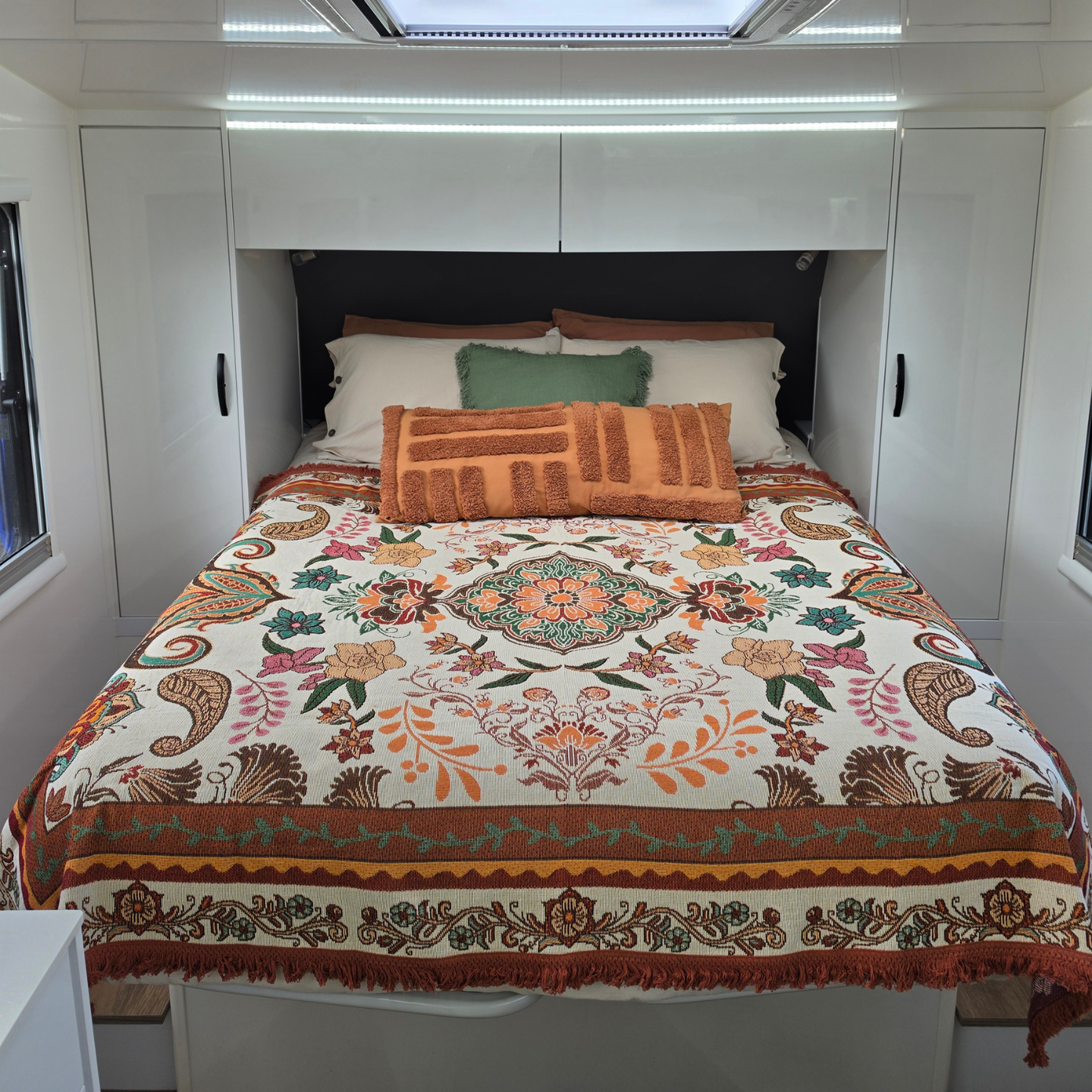 Vanaway Sahara woven travel throw rug featuring a cream, terracotta, sage green and blush boho botanical design, styled as a decorative bed throw inside a modern caravan.