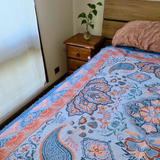 Vanaway Santorini woven travel throw rug featuring a soft blue, terracotta and cream boho paisley design, styled as a decorative bed throw inside a caravan or camper.