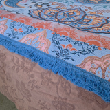 Close up of the Vanaway Santorini woven travel throw rug featuring a soft blue, terracotta and cream boho paisley design with decorative blue fringe edging.