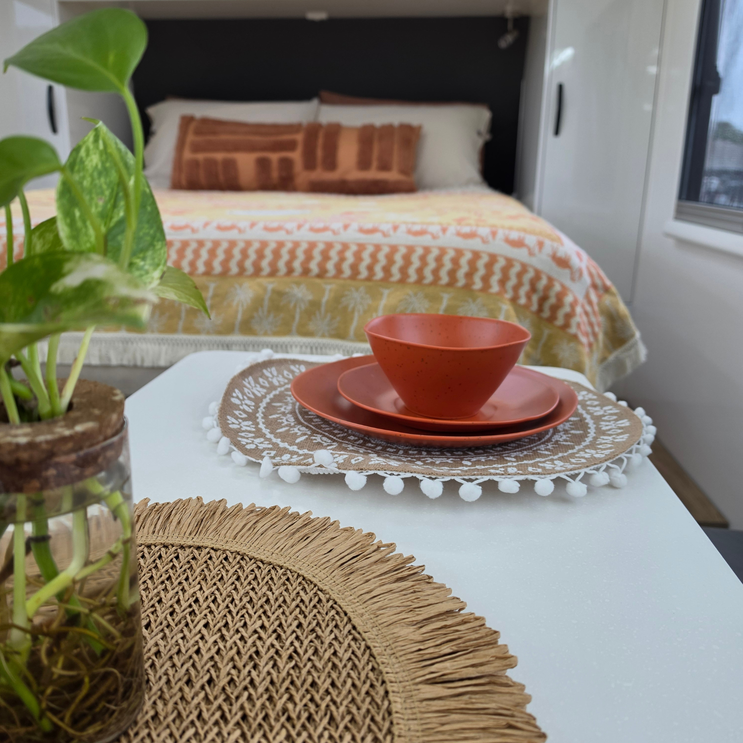 Vanaway Solana woven travel throw rug styled across a caravan bed with Vanaway terracotta dinnerware in the foreground, creating a warm and inviting caravan interior.