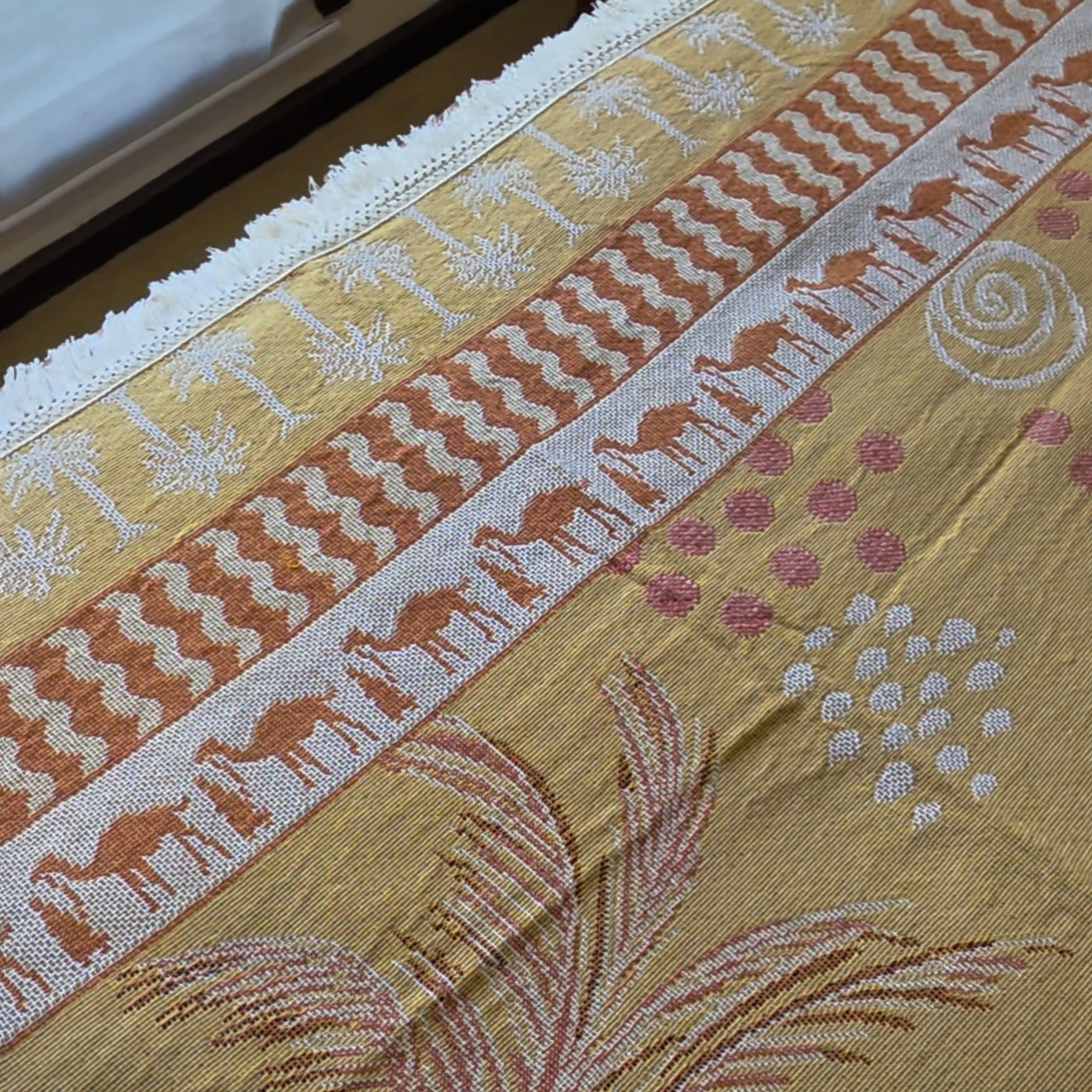Close up of the Vanaway Solana woven travel throw rug showcasing its palm, camel and geometric border pattern with premium woven cotton texture in mustard, blush and cream.