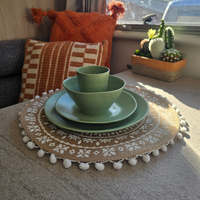 Vanaway Speckled Matcha recycled plastic camping dinnerware featuring a sage green speckled dinner plate, side plate, bowl and tumbler, styled on a woven placemat inside a modern caravan asymmetrical dinnerware