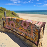 Vanaway Sunblossom woven travel throw rug draped over a beach lookout wall, showcasing the vibrant floral design with the ocean in the background.