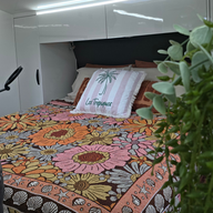 Vanaway Sunblossom woven travel throw rug styled across a caravan bed with floral cushions, creating a warm and colourful caravan interior.