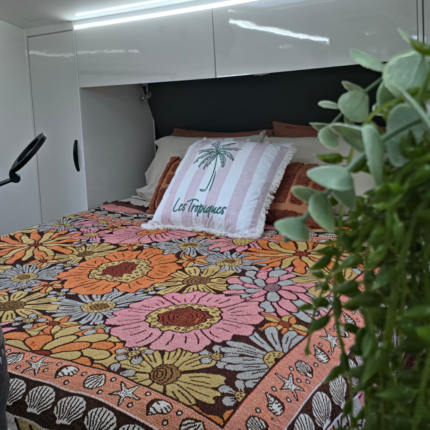 Vanaway Sunblossom woven travel throw rug styled across a caravan bed with floral cushions, creating a warm and colourful caravan interior.