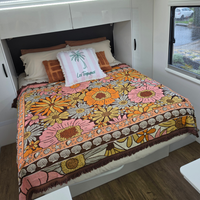 Vanaway Sunblossom woven travel throw rug styled across a caravan bed, showcasing the vibrant floral pattern in a bright caravan bedroom.