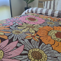 Close-up of the Vanaway Sunblossom woven travel throw rug, showcasing the intricate floral pattern and woven texture styled across a bed.
