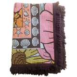 Folded Vanaway Sunblossom woven travel throw rug, showcasing the floral design, woven texture and soft fringe edges.