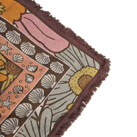 Close-up of the Vanaway Sunblossom woven travel throw rug corner, showcasing the floral border, woven texture and soft fringe detail.