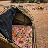 Vanaway Sunblossom woven travel throw rug inside a camping tent with a campfire burning nearby, creating a cosy outdoor camping setup.