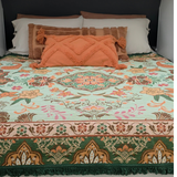Vanaway Willow woven travel throw rug featuring soft blue, sage green, cream and terracotta botanical patterns, styled as a decorative bed throw with earthy cushions inside a modern caravan.