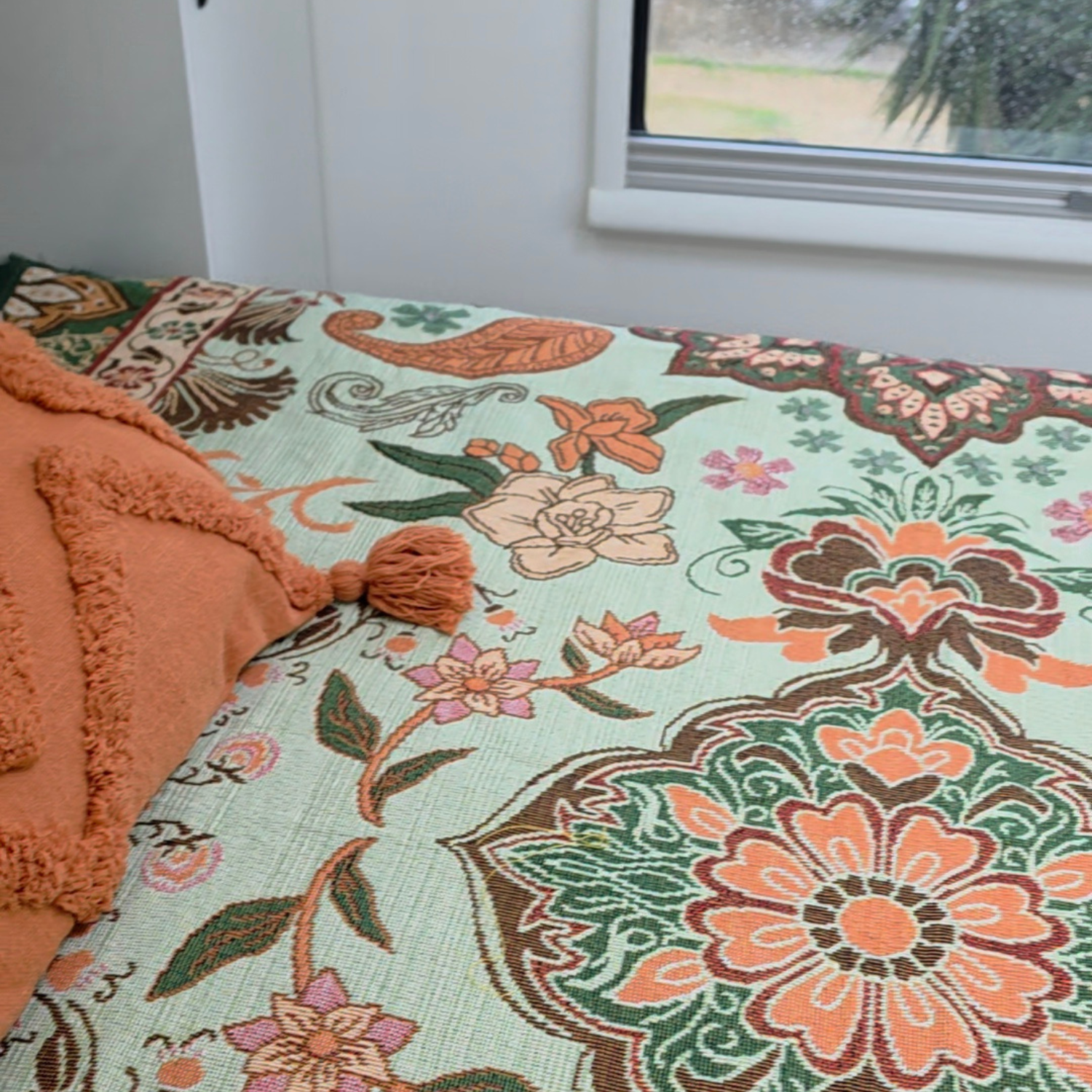 Vanaway Willow woven travel throw rug featuring soft blue, sage green, cream and terracotta botanical patterns, styled as a decorative bed throw inside a modern caravan.