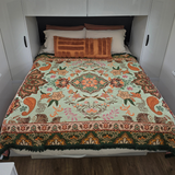 Vanaway Willow woven travel throw rug featuring soft blue, sage green, cream and terracotta botanical patterns, styled as a decorative bed throw inside a modern caravan.