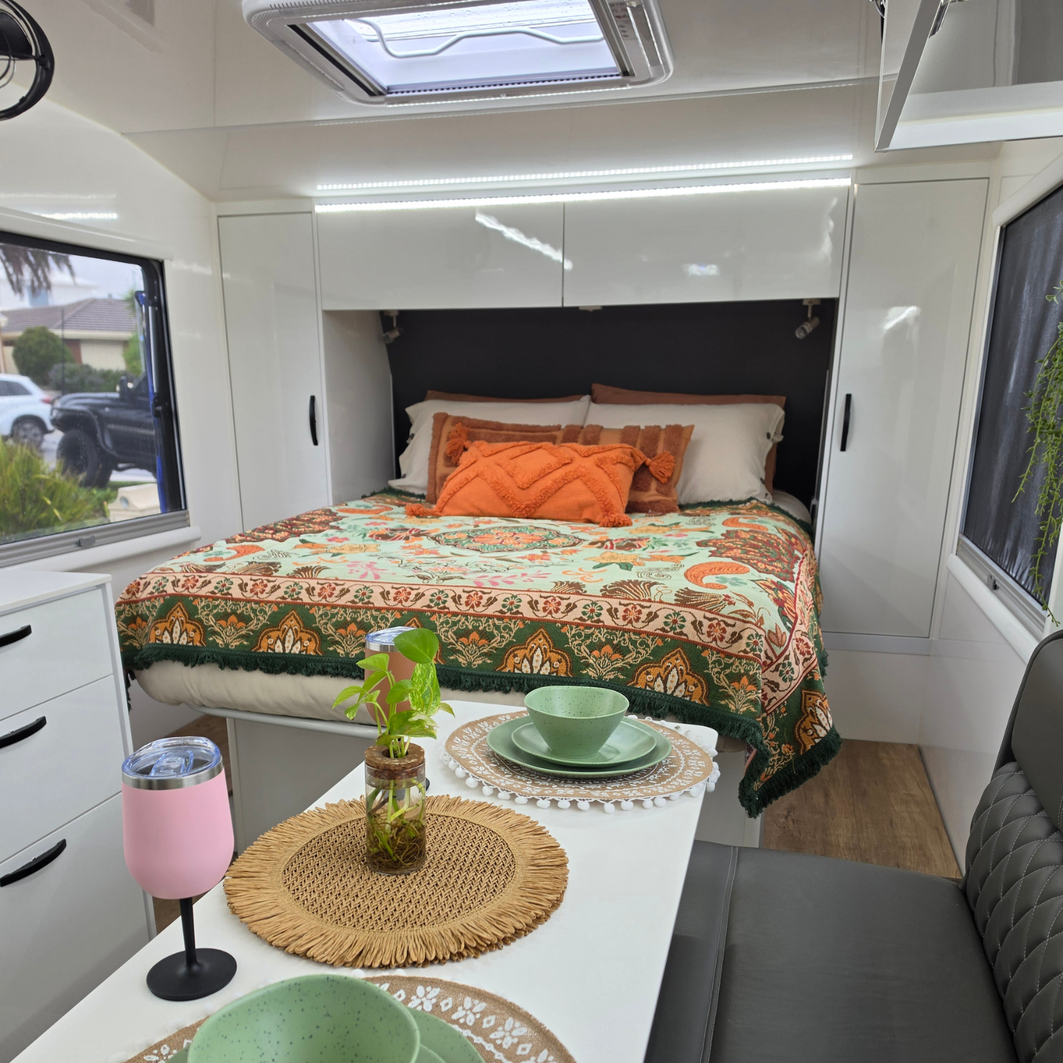 Vanaway Willow woven travel throw rug featuring soft blue, sage green, cream and terracotta botanical patterns, styled inside a modern caravan with matching camping dinnerware and insulated drinkware.