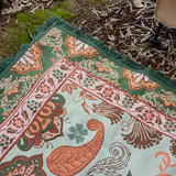 Close up of the Vanaway Willow woven travel throw rug showcasing its soft blue, sage green, cream and terracotta botanical pattern, premium woven texture and decorative green fringe.